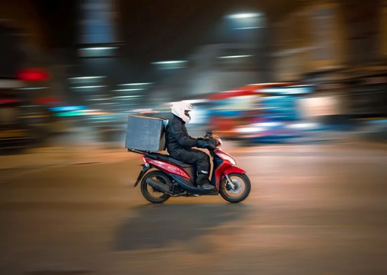 person on moped with delivery bag riding through blurry city streets night